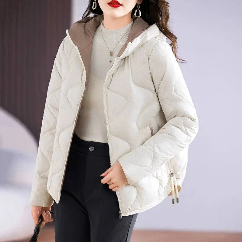Jaqueta puffer feminina em tom creme claro, com capuz e forro interno em contraste marrom, acolchoamento exclusivo em losangos e detalhes refinados, ideal para um inverno com elegância e distinção.