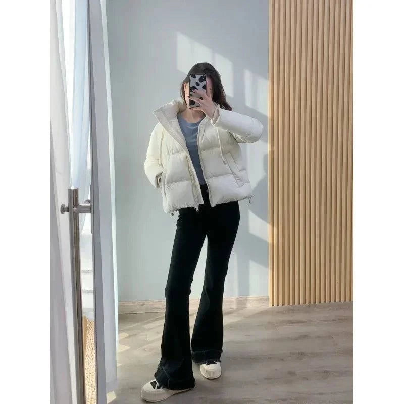 Modelo usando jaqueta puffer feminina creme, com capuz e caimento cropped, combinada com calça preta e tênis, exibindo um look casual de luxo e moderno, perfeito para o inverno.