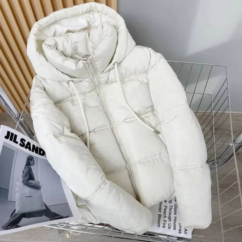 Jaqueta puffer feminina para inverno na cor creme, com capuz e zíper, exibida sobre revista de moda, destacando o acolchoamento e o design luxuoso, ideal para quem busca tendência e exclusividade.