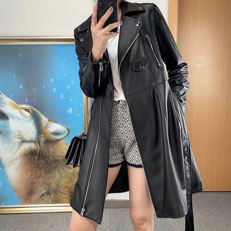 Mulher vestindo Jaqueta Feminina Longa Royal Edge em couro preto com zíperes prateados, bolsos e amarração lateral, combinada com shorts estampados e bolsa a tiracolo, em Embu das Artes, exibindo um estilo de luxo moderno e exclusivo.