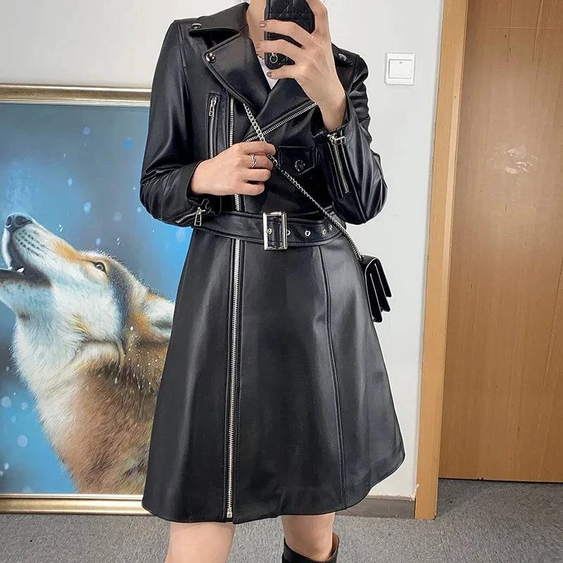 Mulher vestindo Jaqueta Feminina Longa Royal Edge em couro preto, com estilo biker na parte superior e saia evasê, zíperes prateados destacados e cinto com fivela, exibindo um visual ousado e luxuoso de alta exclusividade.