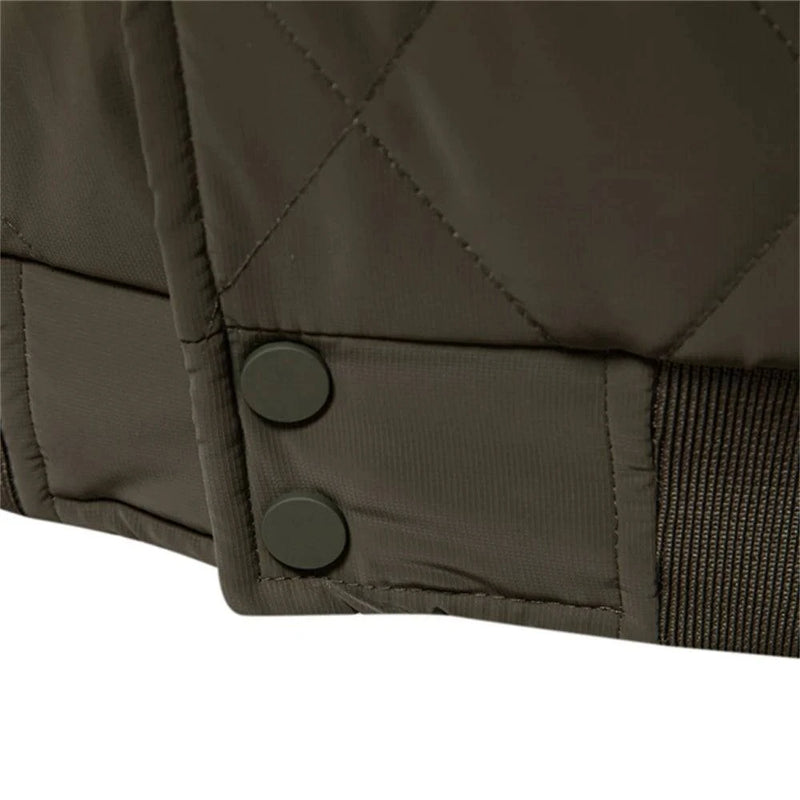 Detalhe aproximado da barra canelada e dos dois botões de pressão na jaqueta masculina bomber acolchoada verde musgo, mostrando o padrão de losangos do tecido. Qualidade no acabamento que denota uma peça cuidadosamente elaborada.