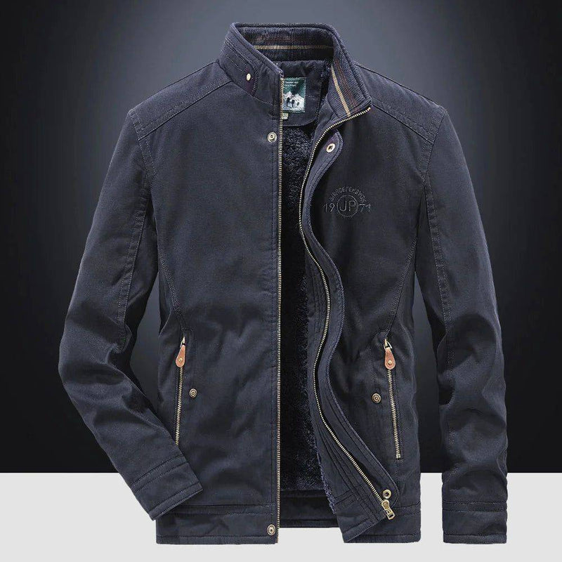 Jaqueta masculina bomber parka azul marinho, aberta revelando o forro de pelúcia preto e a gola alta com detalhes canelados. Os zíperes e botões de pressão, juntamente com o bordado "JP" no peito, conferem um estilo robusto e funcional, ideal para o clima de Embu das Artes