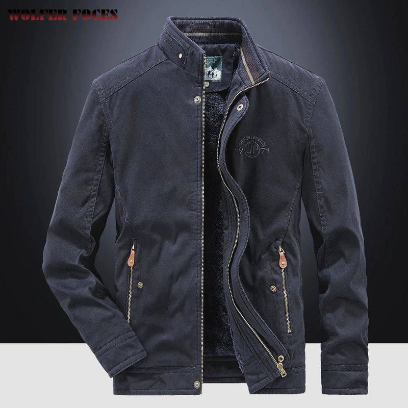 Jaqueta masculina bomber parka azul marinho com gola alta, zíperes duplos (interno e externo), múltiplos bolsos com zíperes e botões de pressão, detalhes em couro marrom nos puxadores, e bordado "DEFENDER 19 JP 71" no peito. O forro de pelúcia preto é visível. Uma peça de alta qualidade e funcionalidade, combinando o estilo militar e o conforto térmico, ideal para o clima de Embu das Artes.