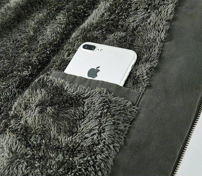 Close-up do bolso interno da jaqueta masculina bomber parka, revelando o forro de pelúcia cinza escuro e um smartphone branco com a maçã mordida visível, parcialmente inserido no bolso. O design prático e o material luxuoso do forro destacam a funcionalidade e o conforto premium da peça.