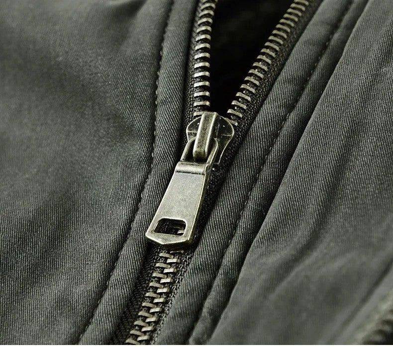 Close-up do zíper frontal da jaqueta masculina bomber parka verde escuro, destacando o cursor metálico em tom envelhecido e os dentes robustos do zíper. A qualidade do hardware sugere a durabilidade e o design premium da peça.
