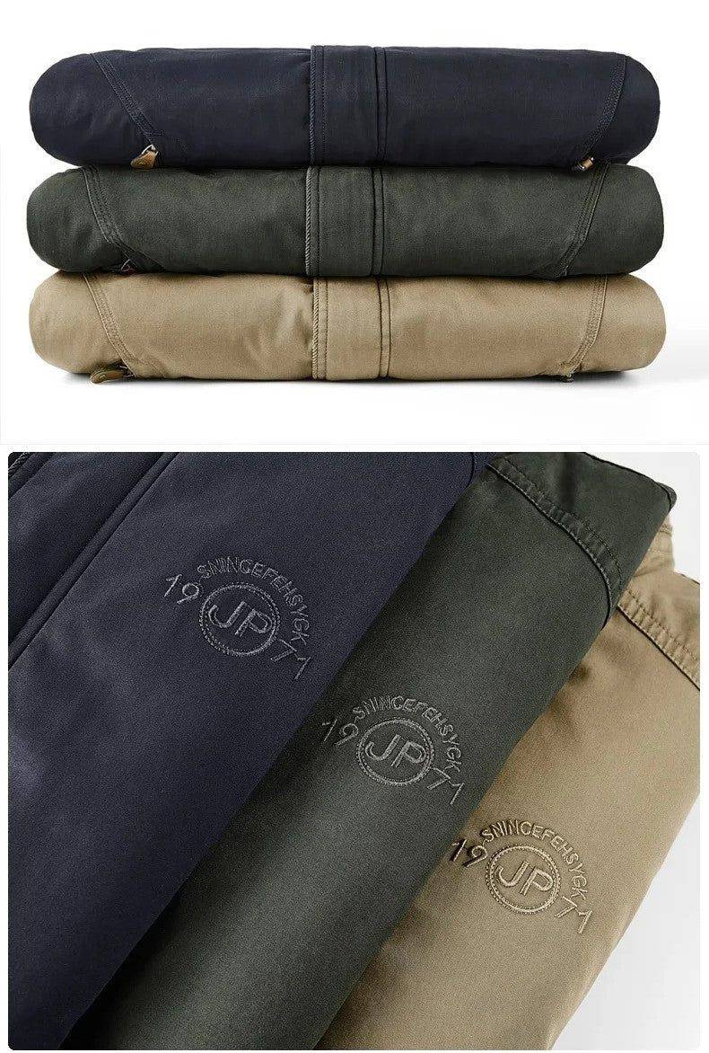 Duas seções da jaqueta masculina bomber parka em três cores: azul marinho, verde musgo e cáqui. A parte superior mostra as jaquetas empilhadas, enquanto a inferior exibe um detalhe do tecido com bordado sutil "SNINGEFEHSIGK 19 (JP) 71". A paleta de cores versátil e o bordado discreto conferem um toque de exclusividade e originalidade para o homem moderno.