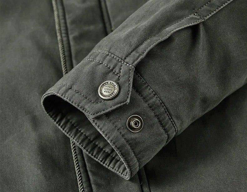 Close-up do punho da jaqueta masculina bomber parka verde escuro, mostrando o detalhe do fecho com botão de pressão, a alça com botão metálico gravado "SPIRIT" e a costura robusta. O acabamento de alta qualidade e o design funcional garantem durabilidade e um toque de exclusividade.