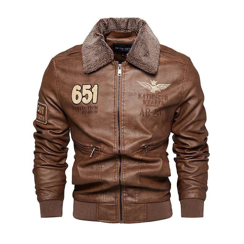 Jaqueta masculina de couro marrom, estilo clássica rider, com gola de pele sintética marrom acinzentada, zíper frontal, múltiplos bolsos e patches bordados, incluindo "651 COLLECTION FASHION" e um emblema de asas com coroa. Punhos e barra canelados marrons. Peça de design robusto e autêntico, conferindo um estilo exclusivo para entusiastas de motociclismo