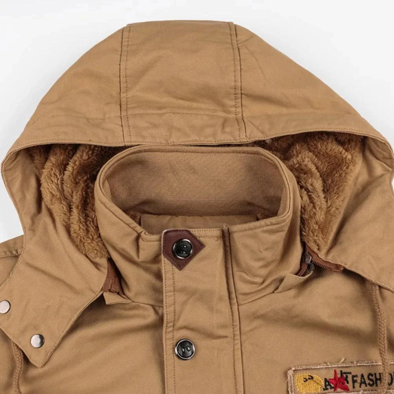 Detalhe aproximado da jaqueta militar forrada caqui, focando no capuz com forro de pelúcia marrom, gola alta e fechamento com botões. O acabamento robusto e o design funcional garantem conforto e um toque de exclusividade para o clima de Embu das Artes.