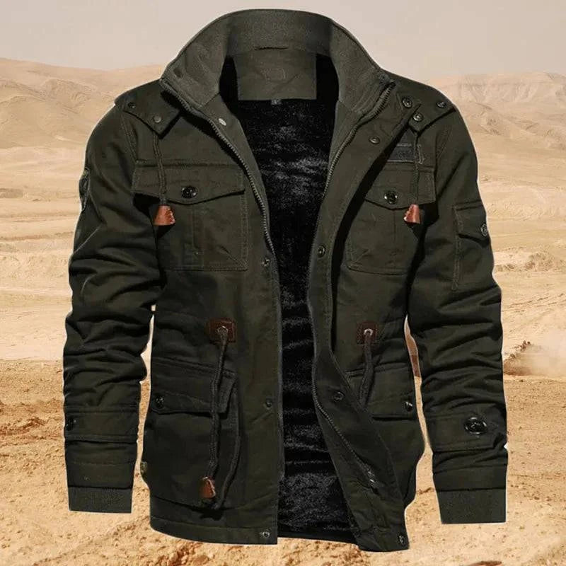 Jaqueta masculina militar forrada em verde musgo, com múltiplos bolsos utilitários, detalhes em couro marrom e cordões ajustáveis, aberta para revelar o forro de pelúcia escuro. Apresentada em um cenário desértico, esta peça robusta e funcional é um item de privilégio para exploradores e entusiastas do estilo outdoor.