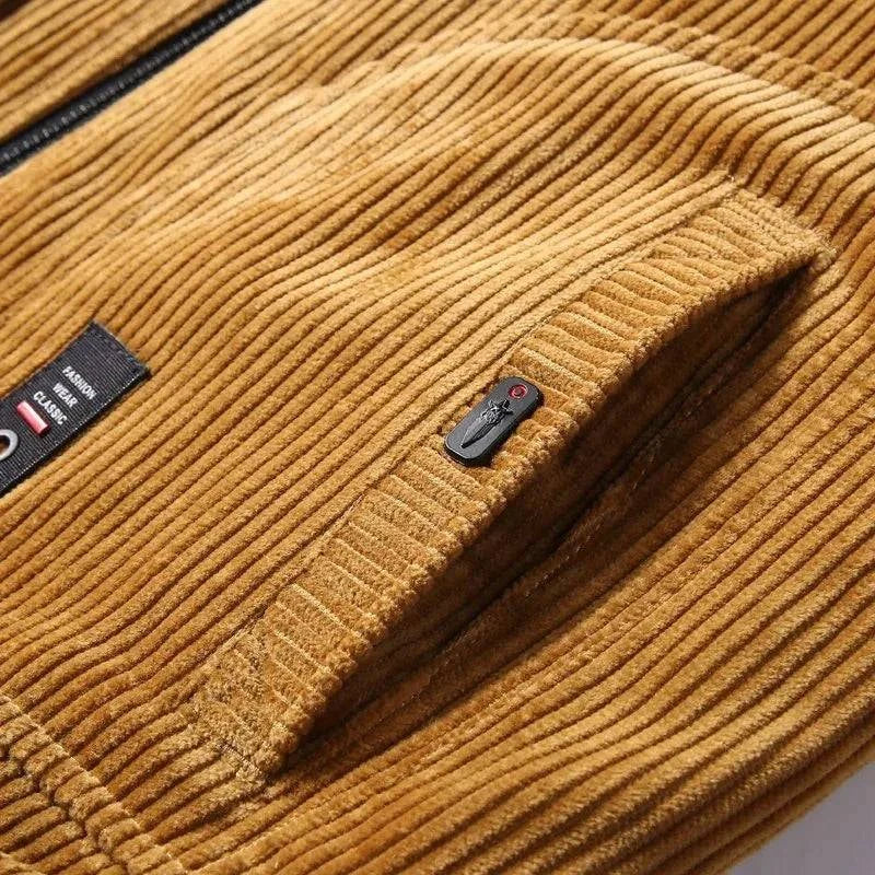 Detalhe aproximado do bolso lateral da jaqueta de veludo cotelê marrom claro, com acabamento em tecido texturizado e um puxador de zíper decorativo em preto e vermelho. A textura do veludo e a etiqueta "FASHION WEAR CLASSIC" ressaltam o design atemporal e a qualidade premium da peça.