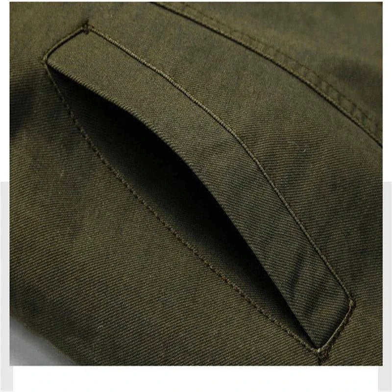 Detalhe aproximado do bolso lateral na jaqueta militar tática verde oliva, com abertura discreta e costuras reforçadas. Design prático e integrado ao tecido, mantendo a estética robusta.