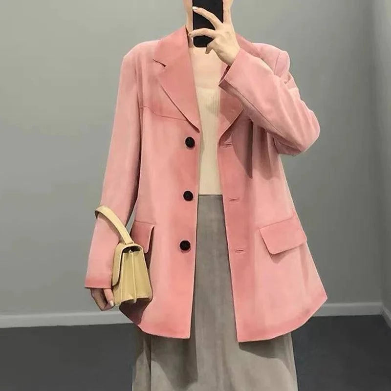 Mulher usando jaqueta de pele de carneiro vintage feminina rosa-salmão, estilo blazer com botões pretos e bolsos frontais, segurando bolsa creme, conferindo um visual de luxo raro e sofisticado com toque vintage.