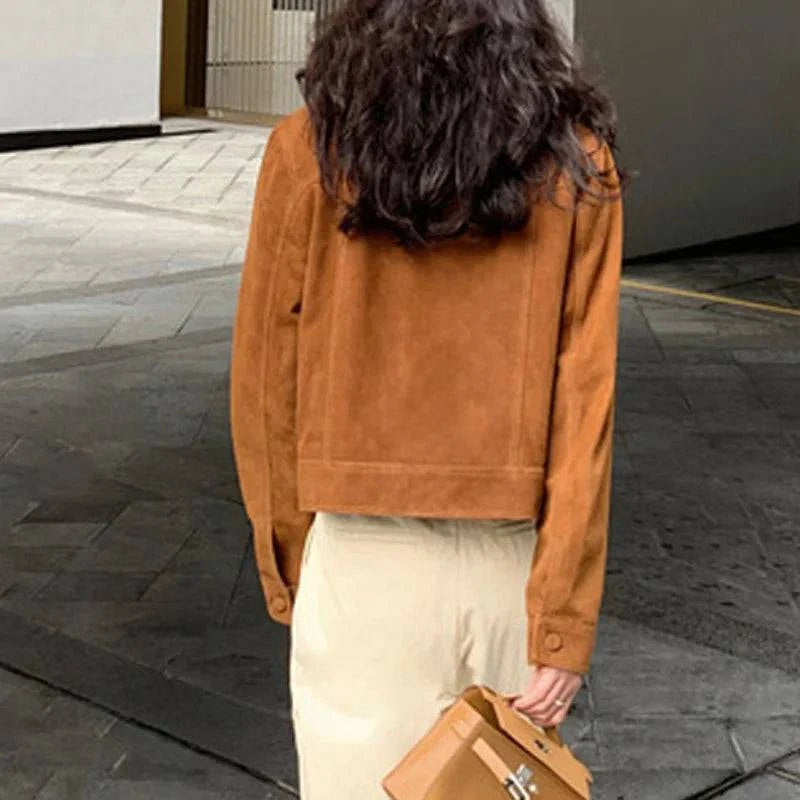 Mulher de costas usando jaqueta feminina de pelo de cabra Hircus na cor caramelo, com barra e punhos ajustados, combinada com calça clara e bolsa, destacando o luxo e a textura aveludada do material exclusivo para o estilo de Embu das Artes.