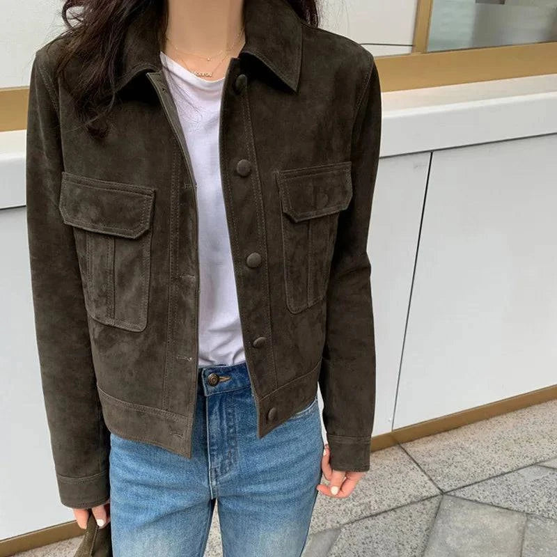 Mulher usando jaqueta feminina de pelo de cabra Hircus na cor marrom-esverdeado, estilo camisa cropped com bolsos de aba e botões, combinada com camiseta branca e jeans, exibindo um luxo discreto e exclusivo para o estilo urbano de Embu das Artes.