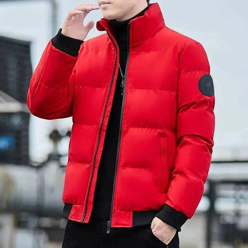 Homem usando jaqueta puffer acolchoada vermelha vibrante com gola alta e fechamento em zíper preto, com punhos e barra canelados pretos e um distintivo circular escuro na manga esquerda. Peça de destaque e conforto excepcional para o inverno.