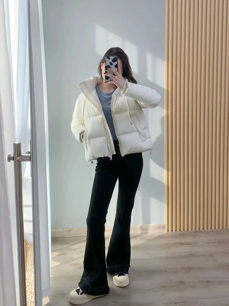 Modelo usando jaqueta puffer feminina creme, com gola alta e caimento cropped, combinada com calça preta e tênis, exibindo um visual de luxo sutil e moderno para o dia a dia.