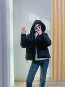 Mulher usando jaqueta puffer preta com capuz, jeans e suéter branco, tirand selfie
