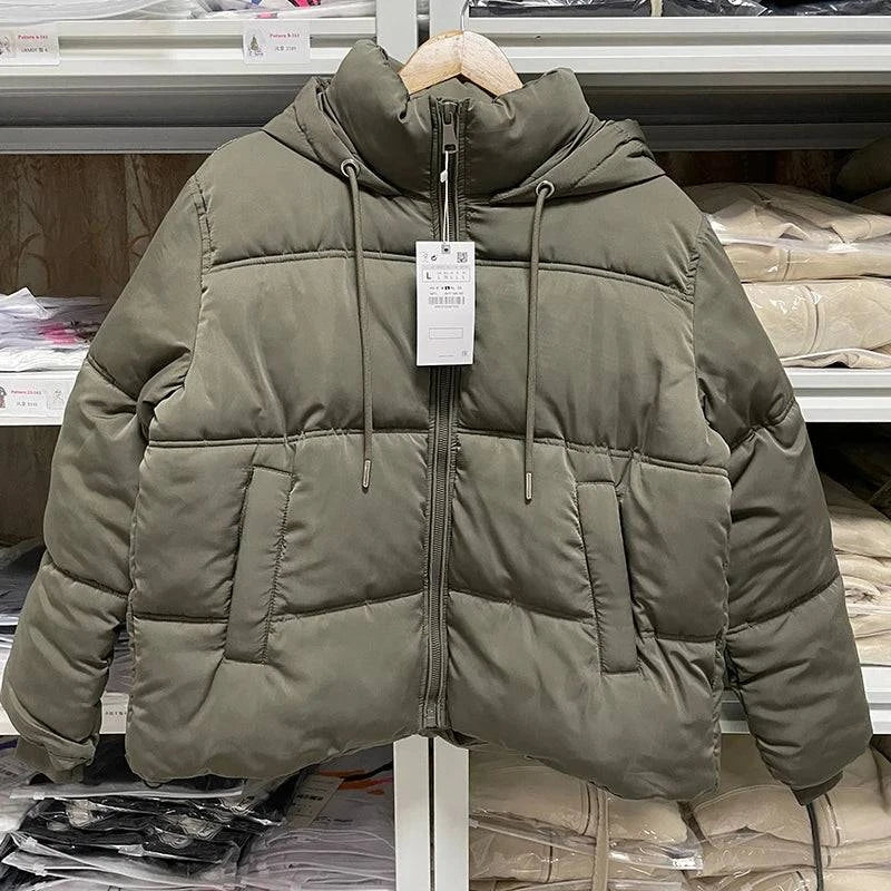 Jaqueta puffer feminina verde militar, com capuz e cordões, acolchoamento térmico e zíper frontal, exibindo um estilo utilitário de luxo e aquecimento essencial para o inverno.