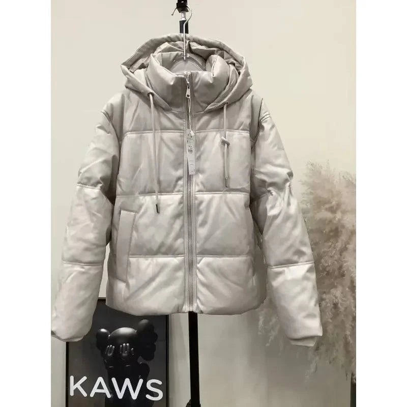 Jaqueta puffer feminina para inverno na cor bege claro, com capuz e zíper, exibindo a etiqueta e os detalhes do acolchoamento, transmitindo qualidade e design moderno.
