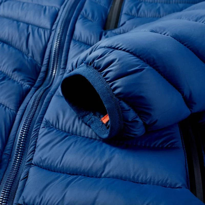 Detalhe do punho da jaqueta puffer masculina azul royal, com acabamento em elástico interno laranja, visível na extremidade da manga. A costura acolchoada e o zíper frontal preto também estão parcialmente à mostra, evidenciando o design funcional e a qualidade da peça para o inverno em Embu das Artes.