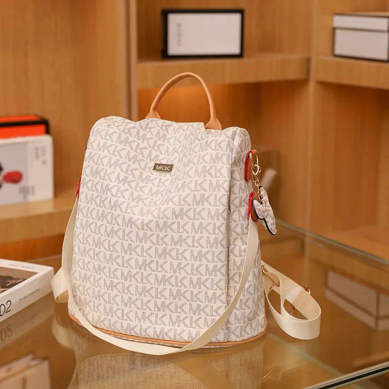 Mochila de couro feminina Travel branca com estampa de monograma "MK" e detalhes em vermelho e bege, exibida em uma prateleira com itens de decoração, destacando seu estilo elegante.