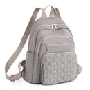 Mochila feminina pequena de nylon cinza, com bolso frontal acolchoado e tachas douradas em relevo, múltiplos compartimentos com zíperes dourados e alças de ombro ajustáveis.