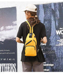 Modelo de costas usando mochila transversal pequena de nylon amarela, com alça única e bolsos laterais de tela, ideal para atividades urbanas.