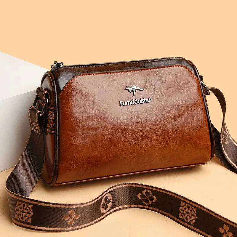 Shoulder Bag Bolsa Feminina de Couro marrom-caramelo. Design de dois tons, logo metálico de canguru e alça estampada larga. Elegante e versátil.