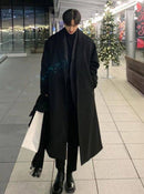 Homem usando sobretudo longo preto com gola alta e cachecol, em corredor de shopping com decoração natalina