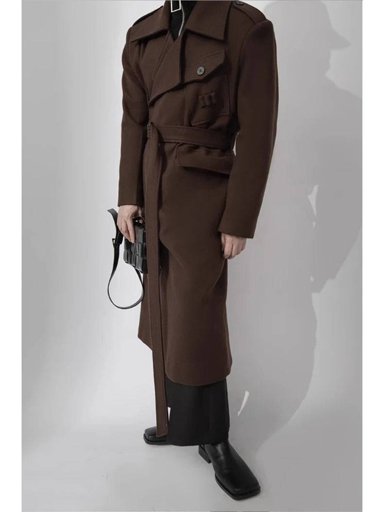 Casaco longo masculino marrom com cinto, usado com calça preta e bolsa, ideal para moda clássica e elegante.