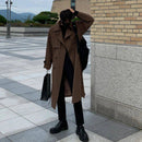 Trench coat longo marrom sobre gola alta preta, com sacola preta, em ambiente urbano.