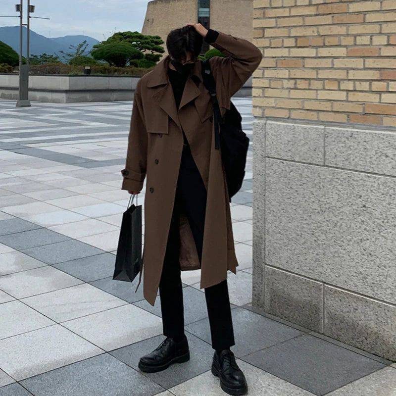 Sobretudo masculino Zellum longo marrom liso, de algodão e poliéster, sobre gola alta preta, com mochila e sacola de compras, em ambiente urbano moderno.