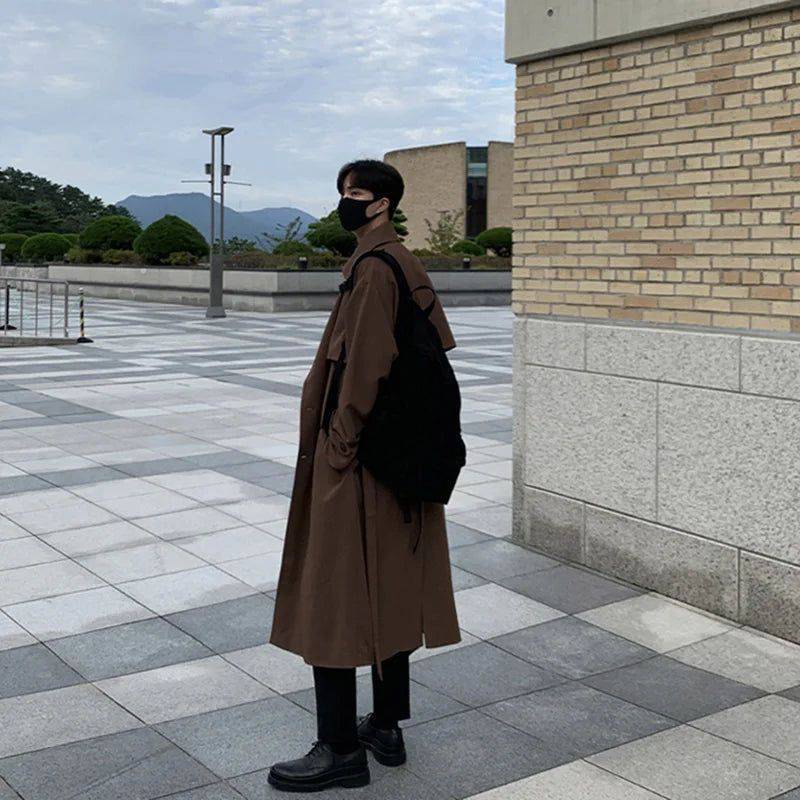 Costas do sobretudo masculino Zellum longo marrom liso, de algodão e poliéster, com mochila preta, em ambiente urbano moderno, estilo casual e funcional.