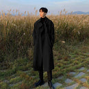 Homem em trench coat preto longo em pé num campo de cereais colhidos