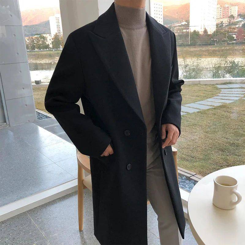 Sobretudo masculino Zellum Longo Mid preto, fechamento duplo, sobre gola alta bege e calça clara, em ambiente com vista para montanhas, evocando elegância e exclusividade.
