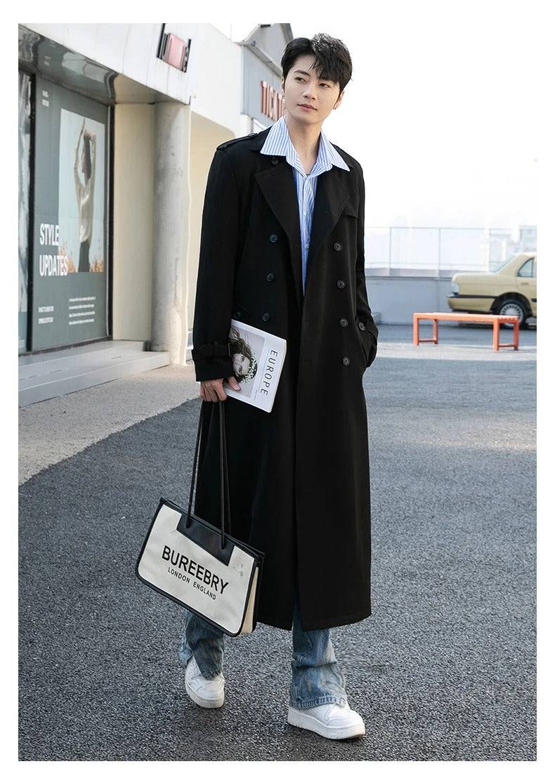 Sobretudo masculino Zellum Premium Elegante preto, longo, com cinto solto, sobre camisa listrada e jeans, em rua urbana, segurando bolsa "Bureebry London England" e revista, estilo sofisticado.