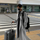 Homem com trench coat cinza solto e mala de viagem em terminal de aeroporto