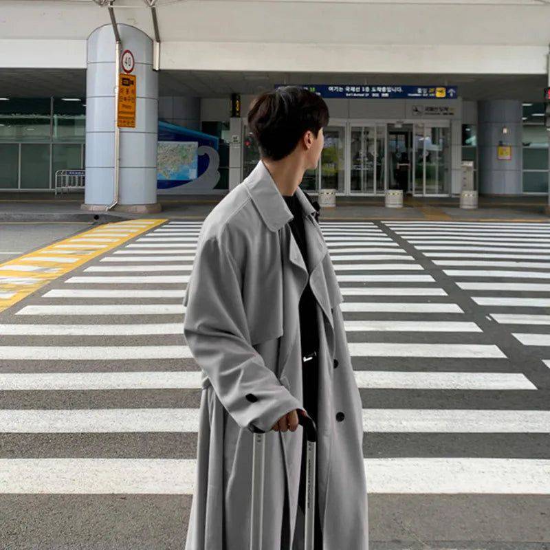 Sobretudo masculino Zellum longo e solto cinza claro, em travessia de pedestres em ambiente urbano, puxando mala de viagem, estilo casual-chique e funcional.