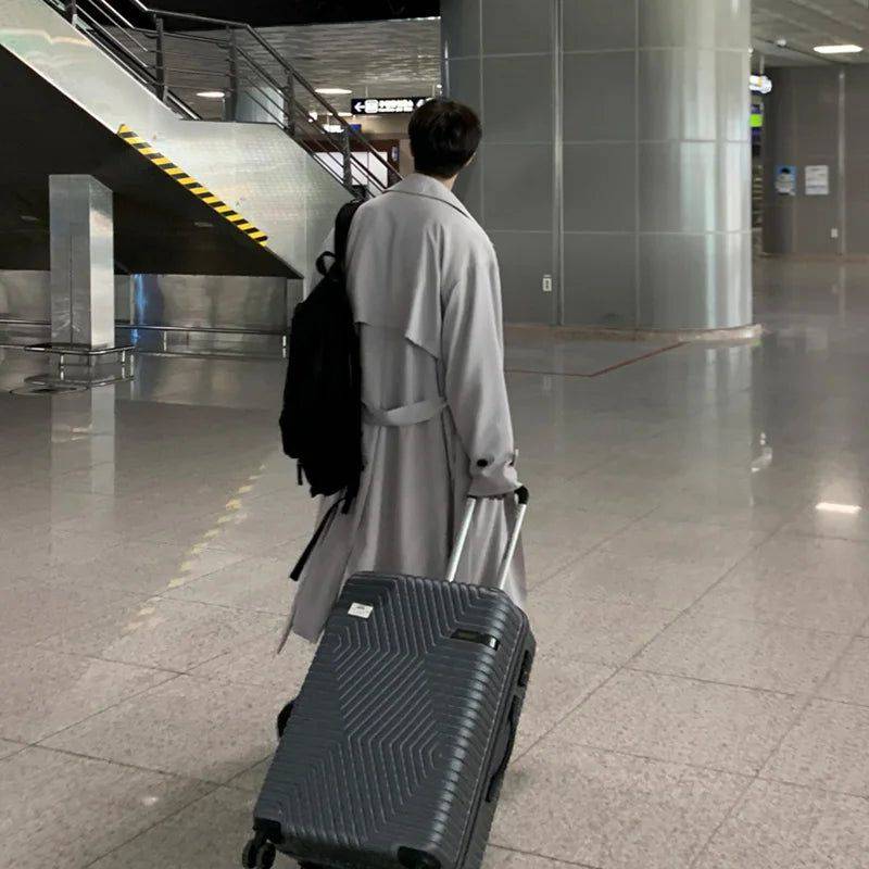 Costas do sobretudo masculino Zellum longo e solto cinza claro, em aeroporto com mala de viagem e mochila, estilo casual e funcional.