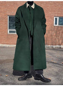 Sobretudo longo verde com gola interna contrastante, paired com camisa preta e botas pretas.