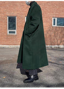 Perfil de homem vestindo sobretudo masculino longo verde, destacando o corte reto e caimento moderno da peça.